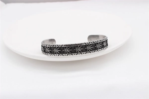 Detailed view of vintage maple leaf engraving on textured steel cuff bracelet