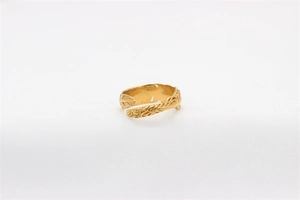Close-up of golden vintage feather ring with detailed carvings on white fabric