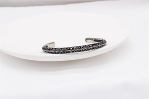 Detailed close-up of retro silver steel cuff with intricate engraved scroll patterns