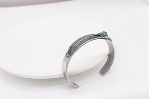 Detail of vintage steel feather cuff bracelet with turquoise stone inlay on white plate