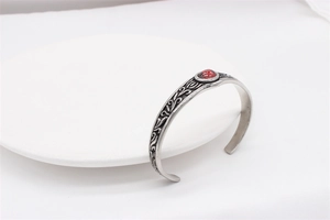 Detailed view of silver cuff bracelet with vintage floral relief and red gemstone