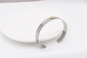 Close-up of silver steel cuff bracelet with a round golden logo on a white ceramic plate