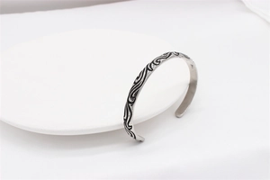 Macro detail of men's vintage steel cuff bracelet with intricate wave pattern engraving