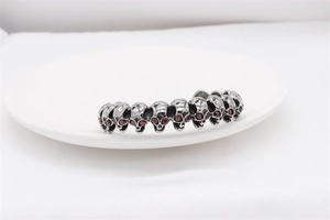 Detailed close-up of retro steel skull cuff bracelet with red gem-set eyes on white plate