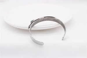 Detail of vintage steel feather cuff with turquoise stone inlay on white ceramic tray