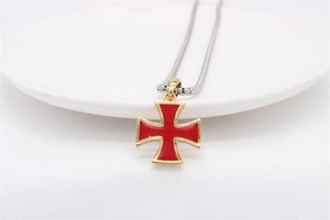 Detail of red enamel cross pendant with gold border displayed on a white plate