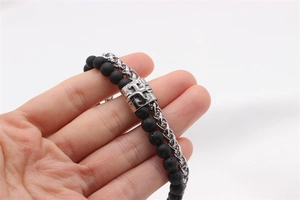 Detail of double-layer beaded bracelet with lava stone and engraved cross metal charm