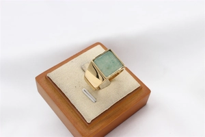 Macro view of gold signet ring with square green gemstone on a jewelry display stand
