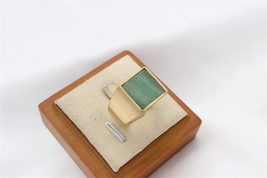 Macro shot of a vintage gold square ring with a rectangular green gemstone on a display stand