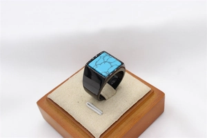 Macro view of men's black stainless steel ring with square turquoise inlay on wood stand