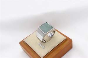 Macro shot of silver signet ring with square green gemstone on a beige cushion display