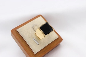 Close-up of a men's gold square signet ring with a large black gemstone on a wooden stand