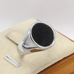 Minimalist silver signet ring with a round black gemstone on a wooden display stand