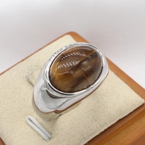 Oval brown tiger eye stone ring in silver stainless steel finish displayed on a stand