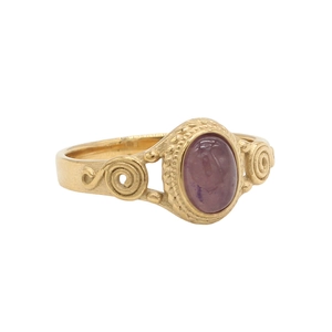 Close-up of vintage gold steel ring with oval purple gemstone and scrollwork details