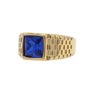 Detalle del anillo dorado con gema azul cuadrada y patrón de tablero en la banda