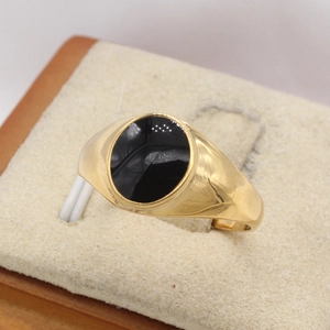 Détail macro d'une bague chevalière dorée avec onyx noir ovale sur un support en velours
