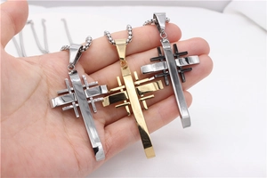 Detailed view of three cross necklaces in gold, silver and black stainless steel colors