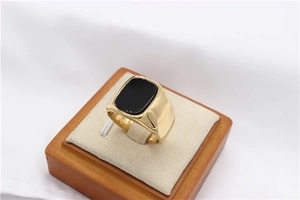 Macro side view of gold signet ring with a rectangular black gemstone inlay on wood display