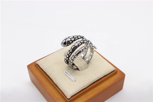 Detalle de anillo de serpiente plateado con texturas de escamas y piedras negras finas