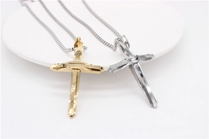 Détail de pendentifs croix géométriques superposés en acier argenté et doré sur plateau