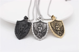 Trois colliers bouclier St Michel en noir, or et argent sur une assiette blanche