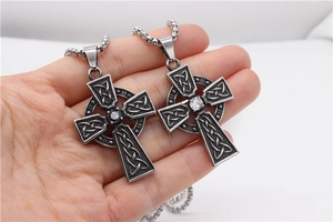 Détails de colliers croix celtique avec pierres noires et claires tenus en main