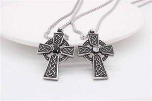 Détail de pendentifs croix celtique avec pierre noire et zircon dans un plat blanc