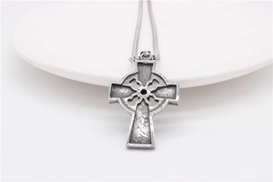 Vue macro du pendentif croix celtique vintage avec nœuds complexes sur plateau blanc