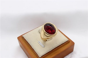 Gros plan d'une bague dorée vintage avec une grande pierre rouge ovale sur un support