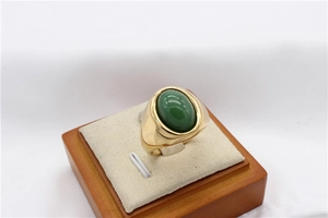 Gros plan d'une bague dorée avec pierre précieuse verte sur un support en bois et fond blanc