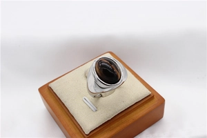 Détail d'une bague large pour homme avec pierre œil de tigre ovale sur un support bois