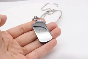 Macro view of polished silver dog tag pendant with industrial style bead chain in hand