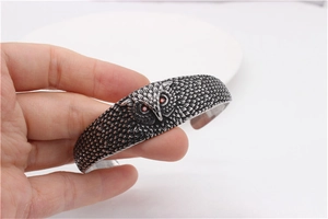 Detailed view of vintage owl head open cuff bracelet with red gemstone eyes and feather texture