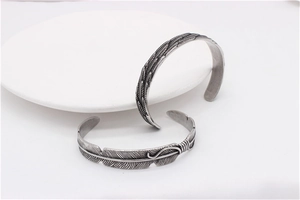 Detailed close-up of retro feather patterned titanium steel bracelets on white tray