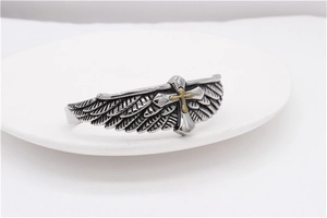 Macro shot of vintage silver eagle wings and a gold cross on an open steel bangle