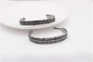 Close-up of vintage feather and Celtic braid steel cuffs on a white ceramic tray