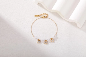 Détail d'un bracelet doré avec perles blanches et breloques carrées sur fond minimaliste