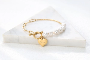 Detail der Goldherz-Anhänger mit Love-Gravur und eleganter Perlenkette auf weißem Marmor