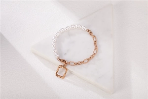 Détail du bracelet chaîne en or rose et perles avec breloque rectangle sur marbre