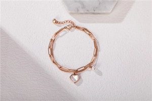 Detail of rose gold layered bracelet with heart mother-of-pearl charm and small pearl