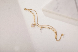Macro detail of gold double-layer chain bracelet with heart mother-of-pearl and pearl charm