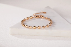 Dettaglio del bracciale a sfere ovali oro rosa con chiusura a moschettone su marmo