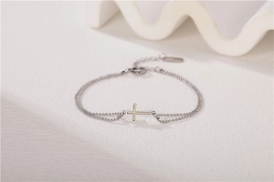Détail d'un bracelet à double chaîne perlée avec un pendentif en forme de croix en nacre