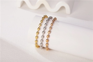 Dettaglio di perline ovali lucide in oro, argento e oro rosa su supporto bianco