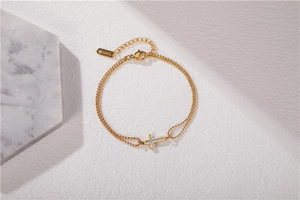Détail d'un bracelet doré double chaîne avec pendentif croix et breloque S.Steel