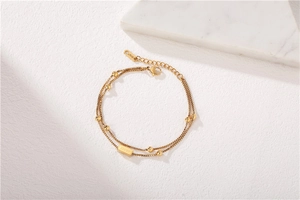 Detail of gold double-layer chain bracelet featuring small beads and a Lucky engraved tag