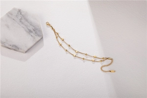 Detail of double-layer gold star anklet with polished beads on a textured surface