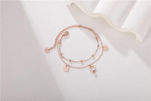 Detail of rose gold double-layer steel bracelet with heart, love disc and ring charms