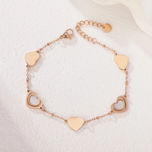 Minimalist rose gold bracelet with heart charms and white shell inlays on stone surface